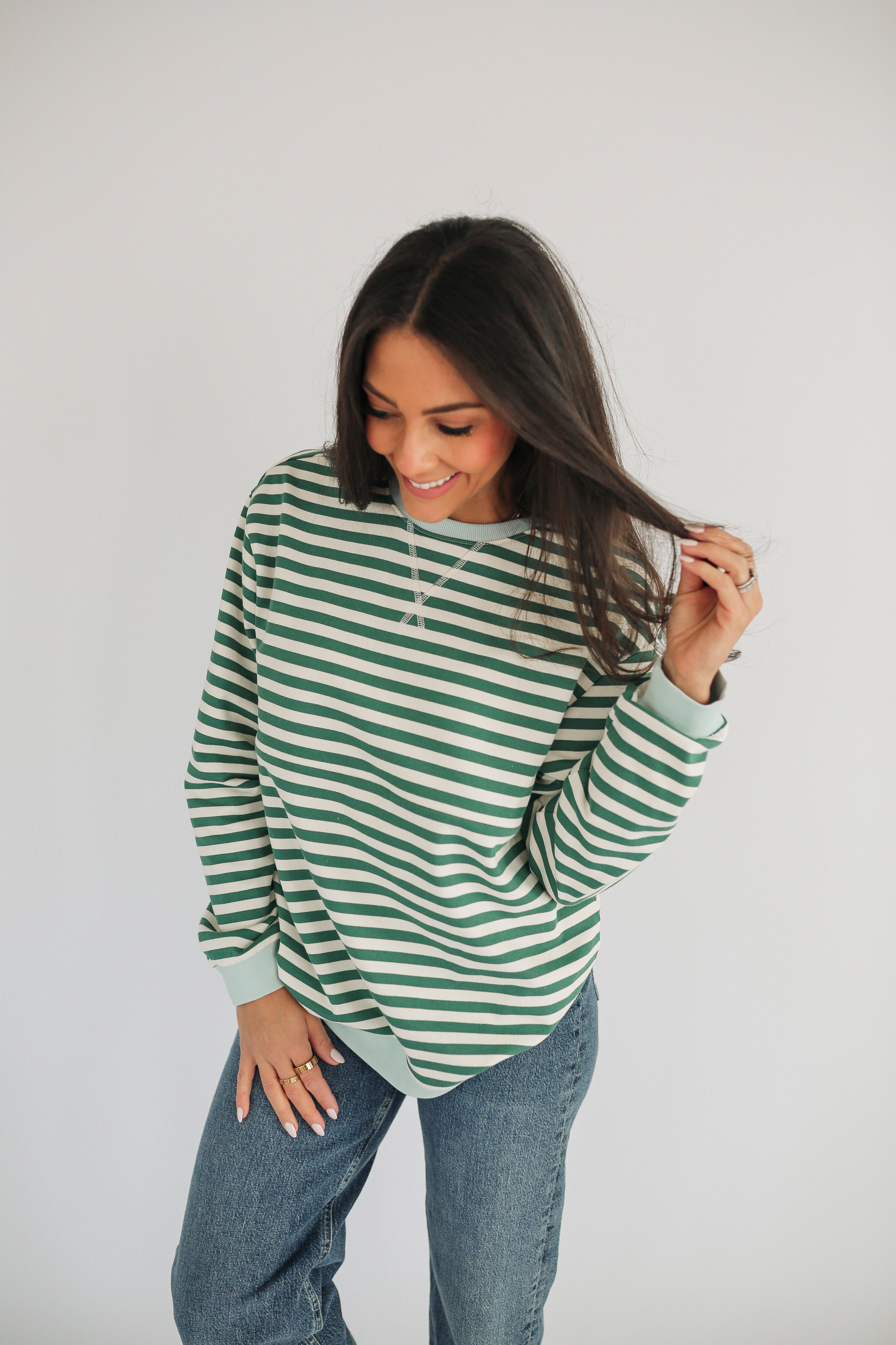 Woman wearing a green and white striped long-sleeve shirt and jeans on a plain background