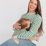 Smiling woman wearing an oversized fit breastfeeding sweatshirt while nursing her baby in a cozy setting.