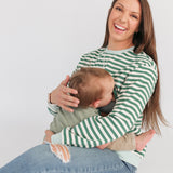 Smiling woman wearing an oversized fit breastfeeding sweatshirt while nursing her baby in a cozy setting.