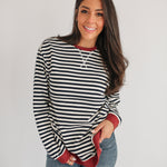Woman wearing a black and white striped shirt with red accents on a plain background