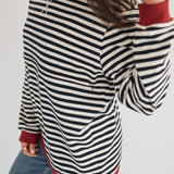 Person wearing a black and white striped sweater with red trim on a plain background