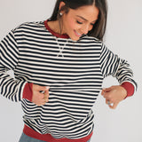 Woman wearing a black and white striped sweater with red trim on a plain background