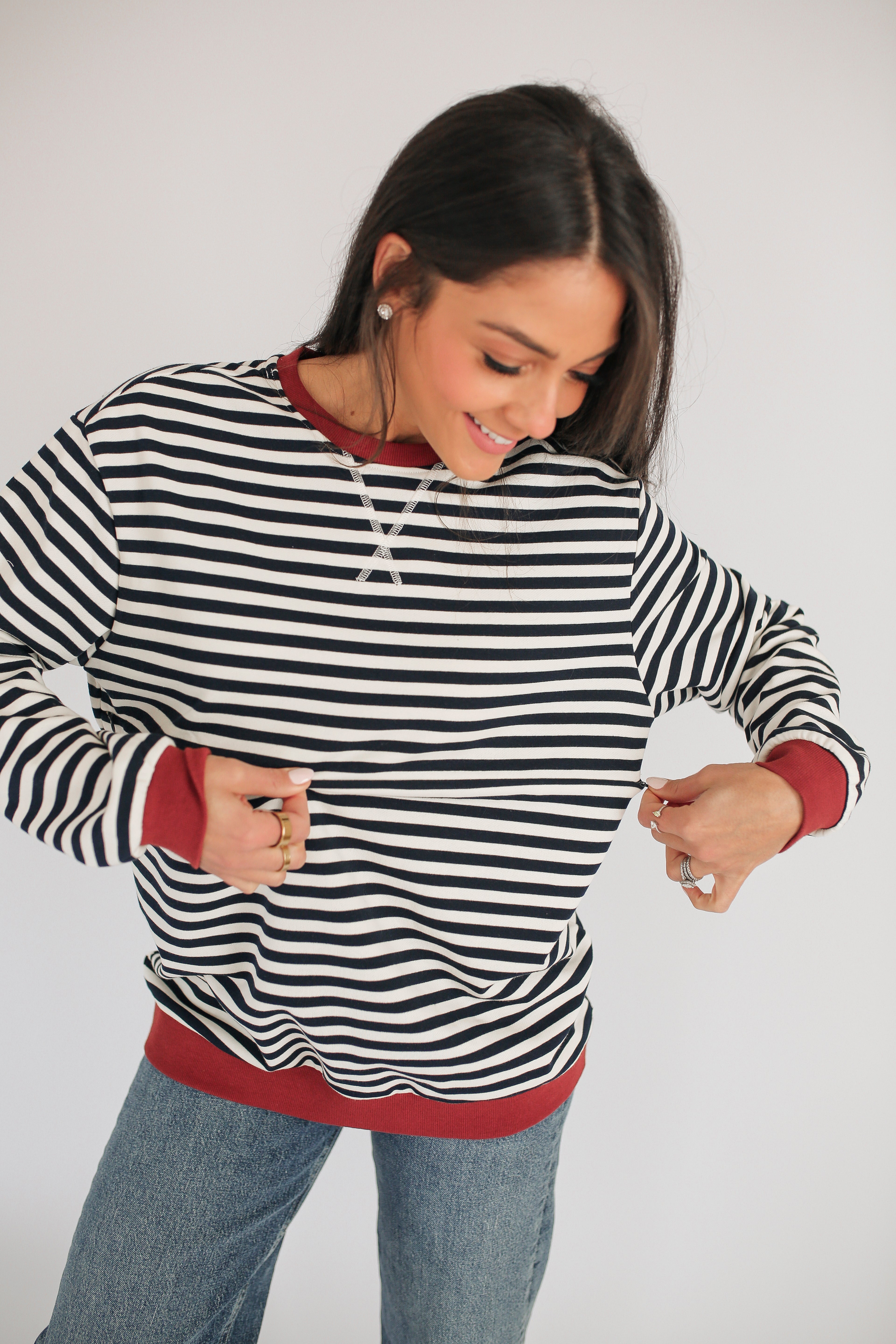 Woman wearing a black and white striped sweater with red trim on a plain background