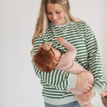 Woman in a green and white striped sweater holding a baby against a plain background