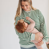 Woman in a green and white striped sweater holding a baby against a plain background