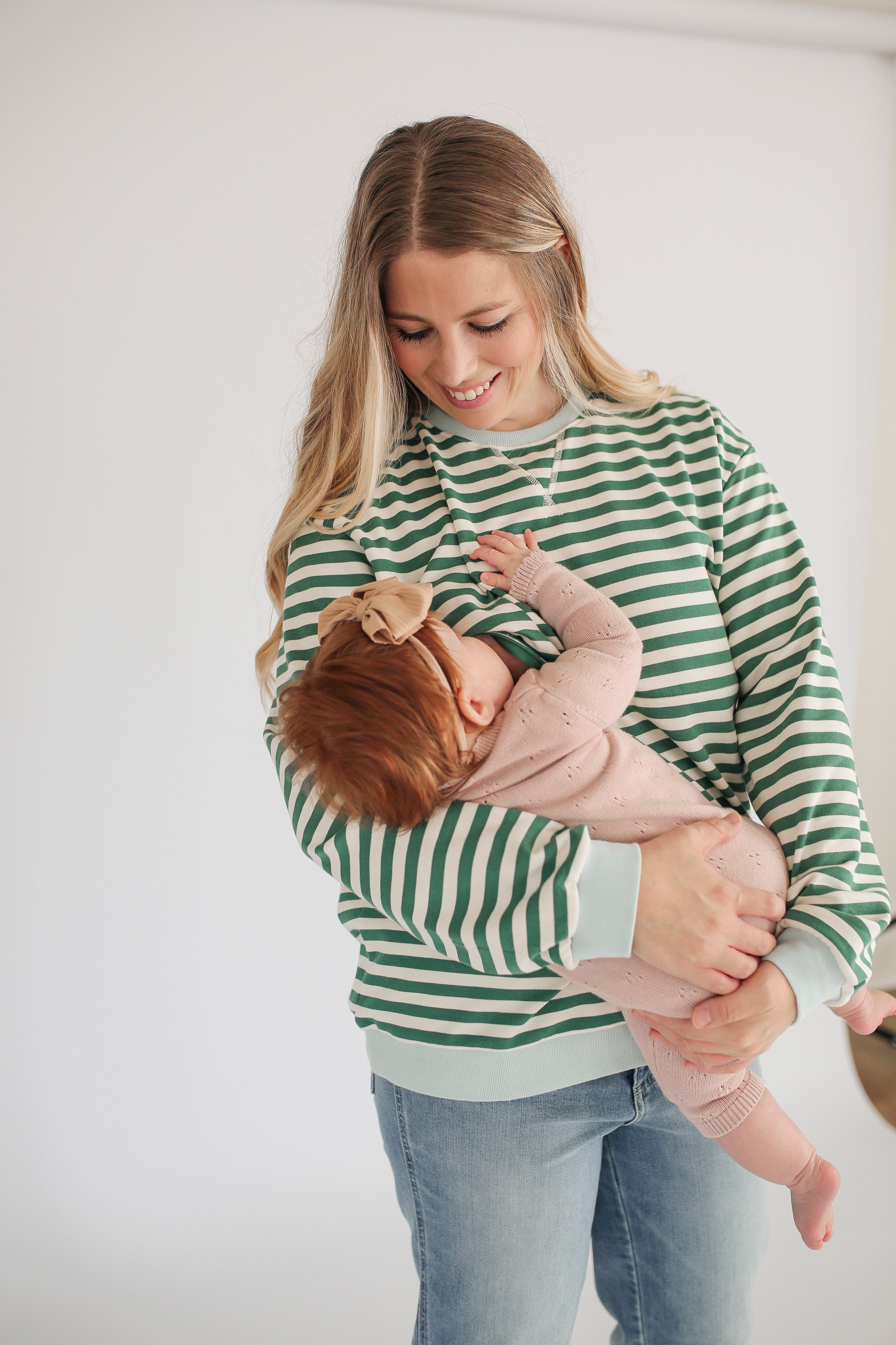 Woman in a green and white striped sweater holding a baby against a plain background