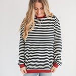 Woman wearing a black and white striped sweater with red trim on a plain background