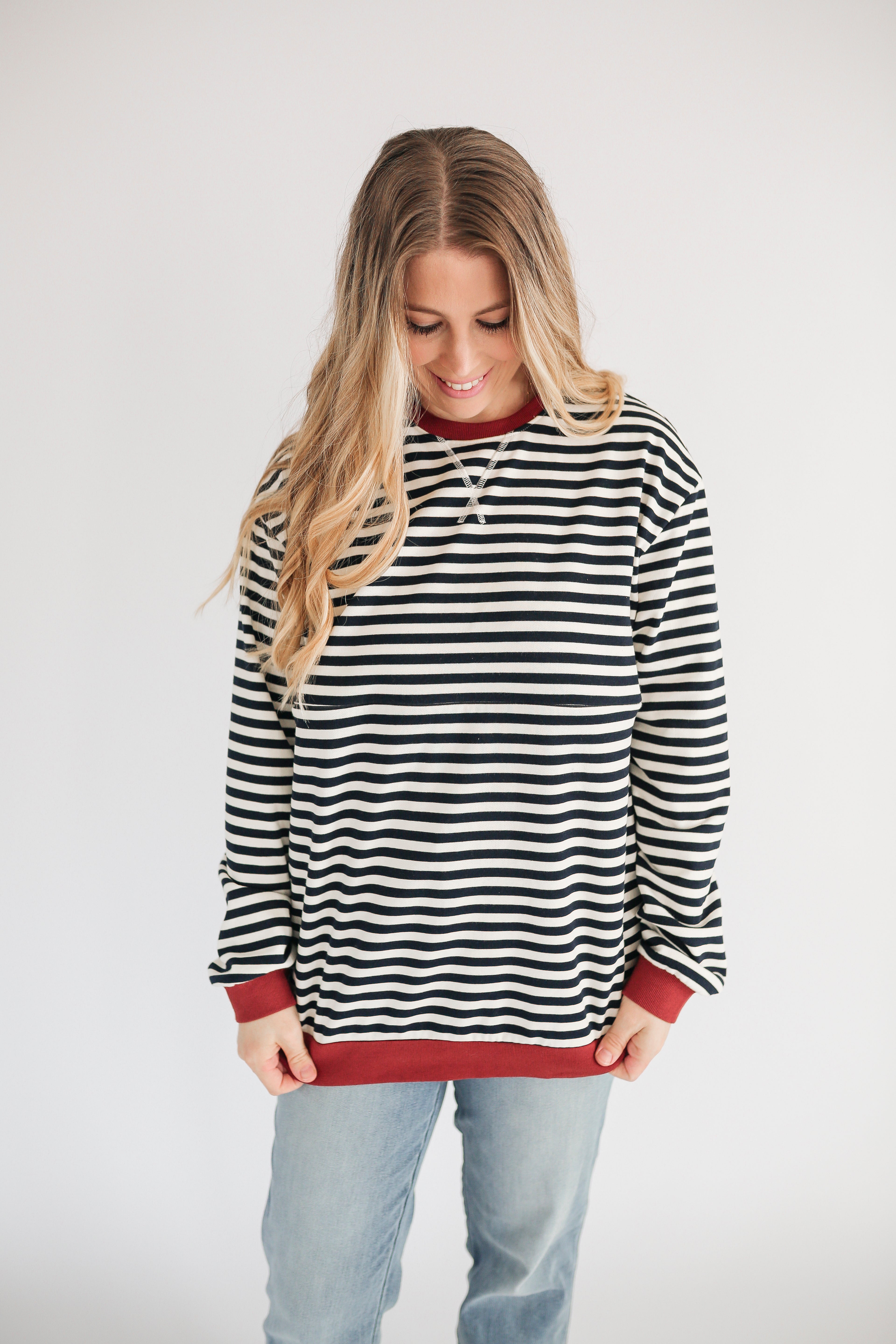 Woman wearing a black and white striped sweater with red trim on a plain background
