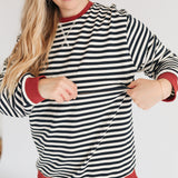 Woman wearing a black and white striped sweater with red trim, smiling and holding the sweater open.