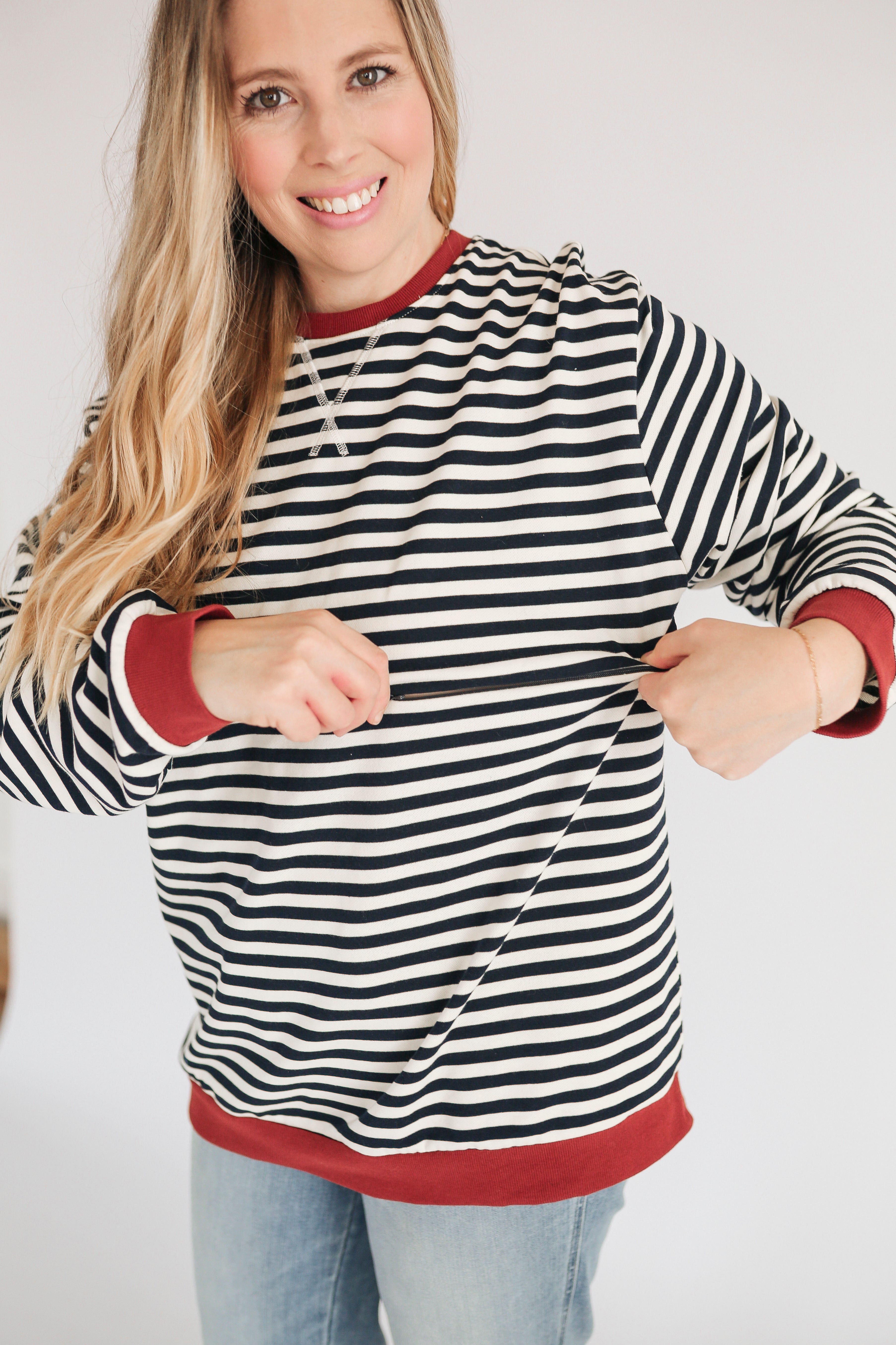 Woman wearing a black and white striped sweater with red trim, smiling and holding the sweater open.