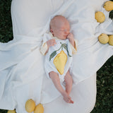 Baby in a lemon-themed onesie lying on a white blanket with lemons around