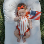 Baby in Picnic Pinstripe | Knit Ruffle Romper holding a small American flag on a sunny day.