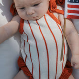 Picnic Pinstripe | Knit Ruffle Romper on baby with soft fabric and ruffle details, holding a small flag.