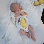 Newborn baby wearing a onesie with lemon design, lying on a white blanket.