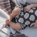 Muslin tank romper on a baby, featuring seashell prints and ruffled edges, perfect for warm weather.