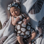 Baby wearing a seashell patterned muslin tank romper and matching headband, relaxing on a soft blanket.
