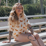 Model wearing Hot Dogs | Women's Bamboo Short Set, featuring a playful hot dog print, sitting on a bench outdoors.