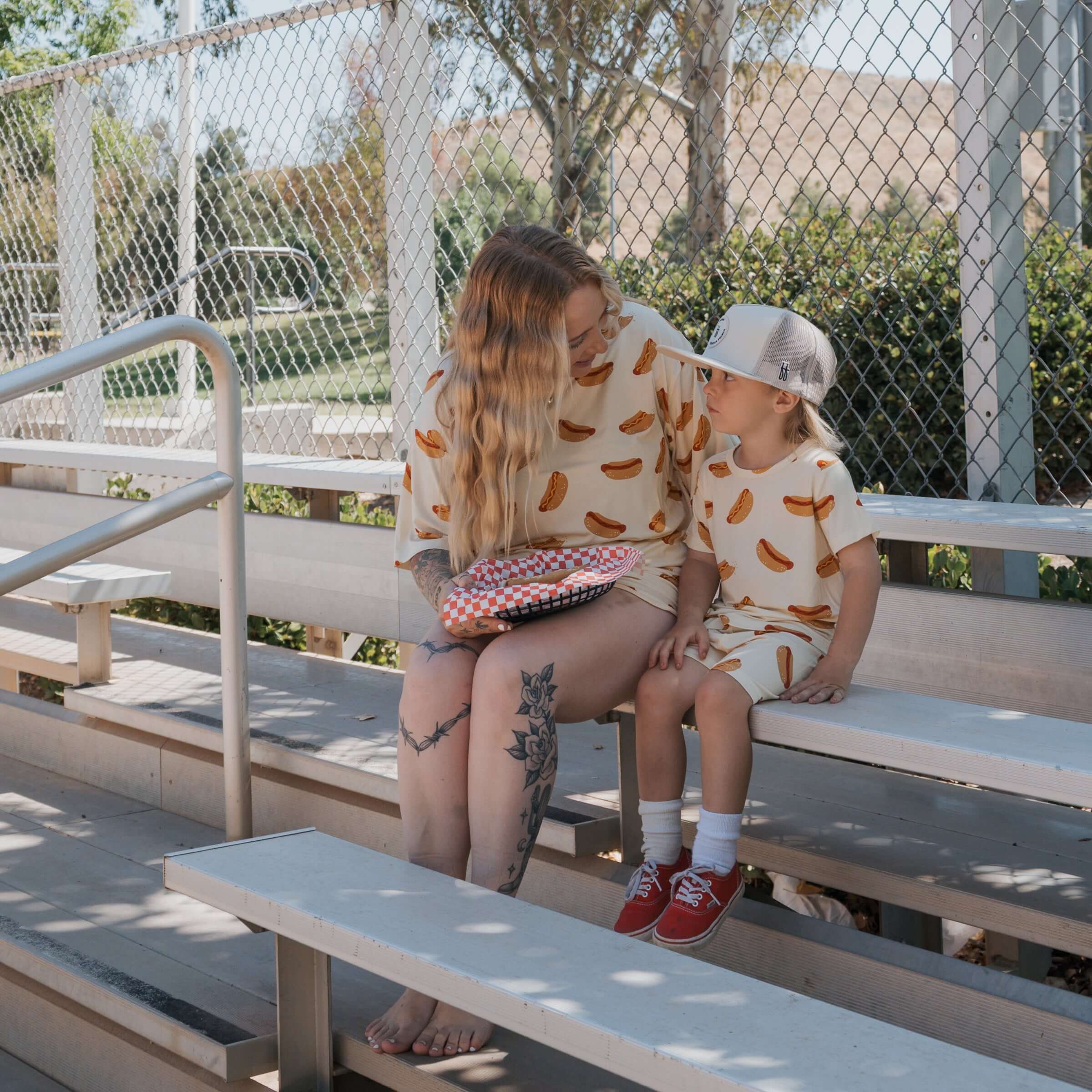 A woman and child sitting on bleachers in matching Hot Dogs | Women's Bamboo Short Set, enjoying the sunny day.
