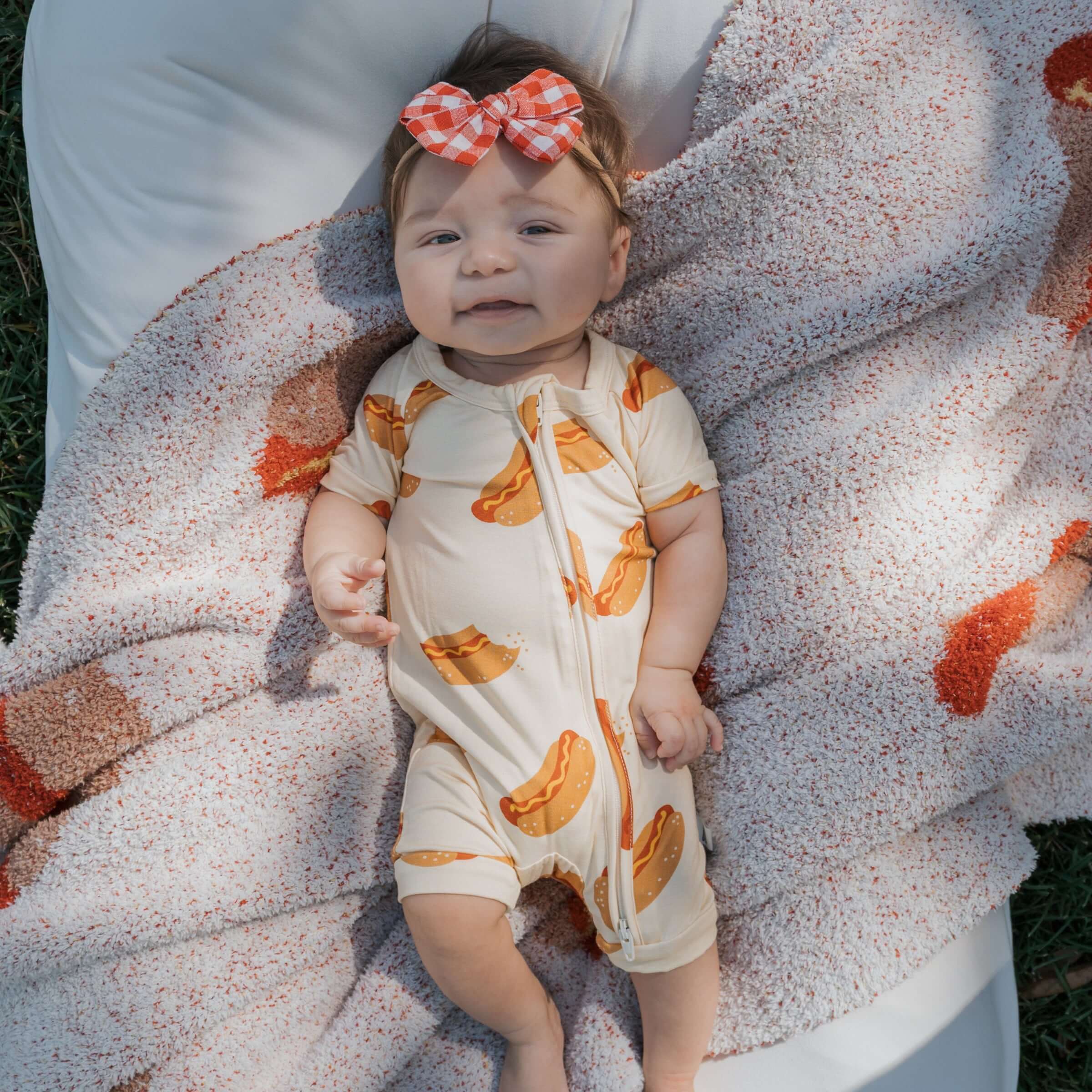 Baby smiling in Hot Dogs | Shortie Bamboo Zip pajamas on a cozy blanket | milk & baby.