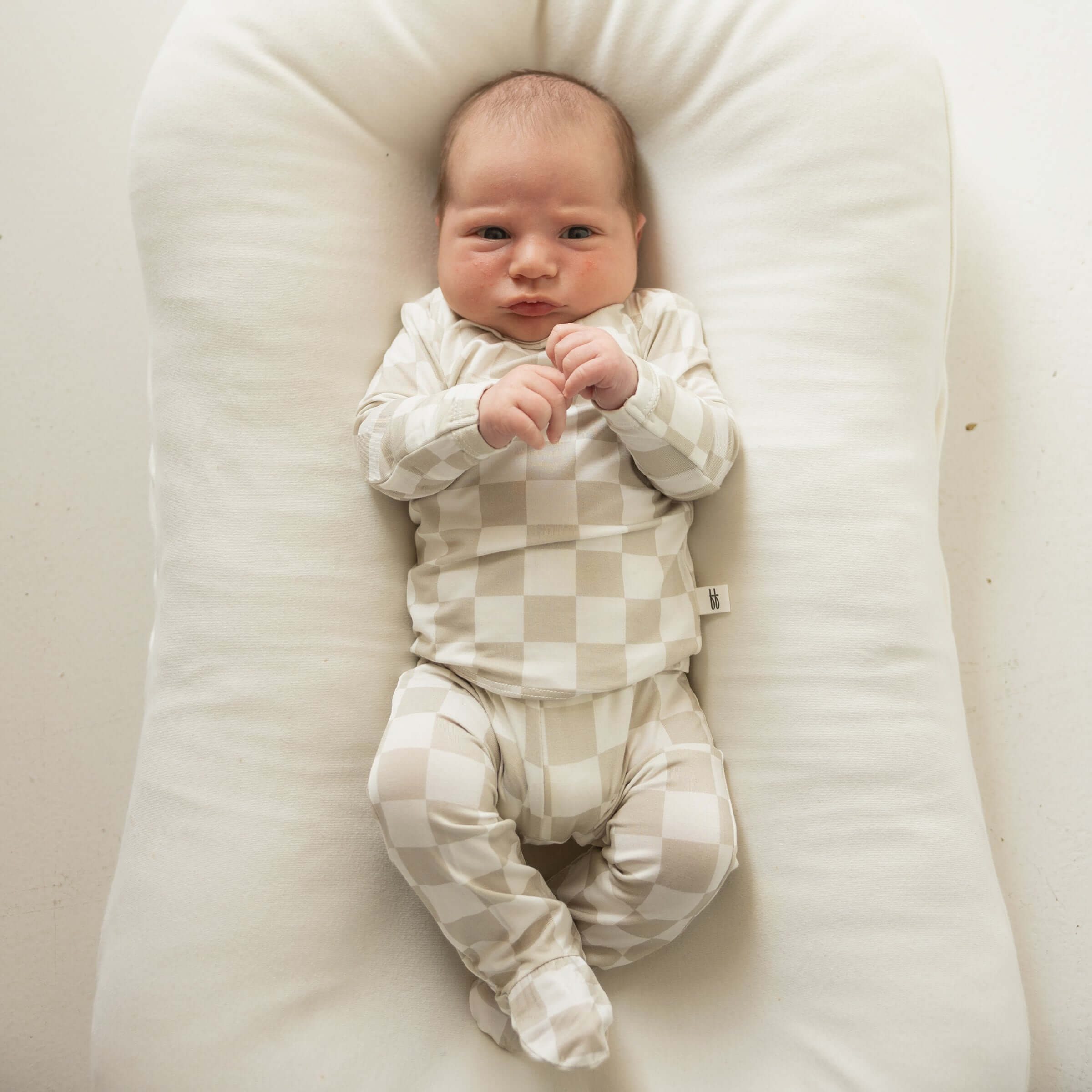 Newborn baby in a checkered outfit lying on a white pillow