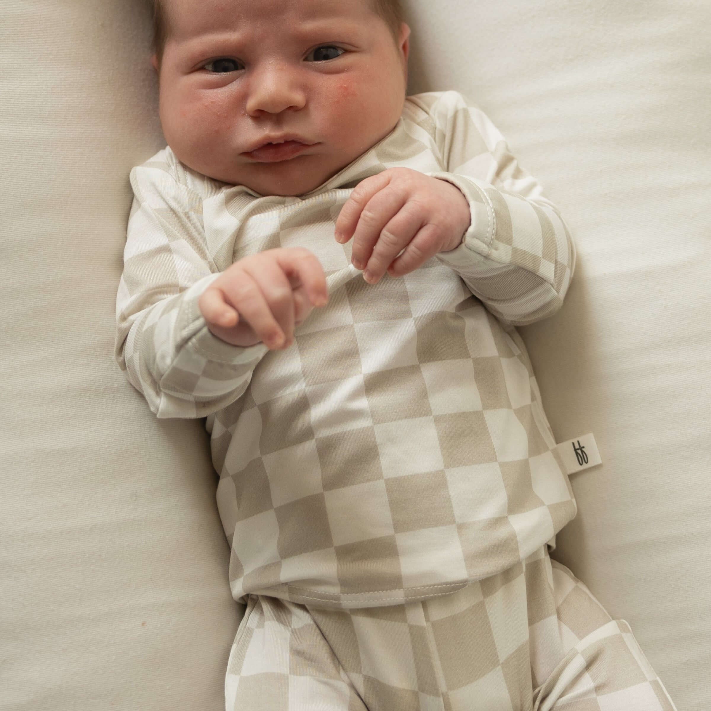 Baby wearing a checkered outfit lying on a soft surface