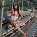 A model wearing a Hot Dogs | Adult Cotton Tee sitting on bleachers, enjoying a sunny day with sunglasses.