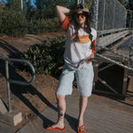A model showcasing the Hot Dogs | Adult Cotton Tee paired with denim shorts and flip-flops in a casual outdoor setting.