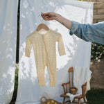 Bamboo Zip Pajamas in yellow hanging on a wooden hanger against a soft background, showcasing the cozy design and durability.