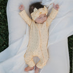 Baby wearing Veda Bamboo Zip Pajamas in yellow with black polka dots, relaxing on a white blanket outdoors.
