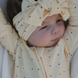 Baby wearing Veda Bamboo Zip Pajamas in soft yellow with black dots, styled with a matching headband.