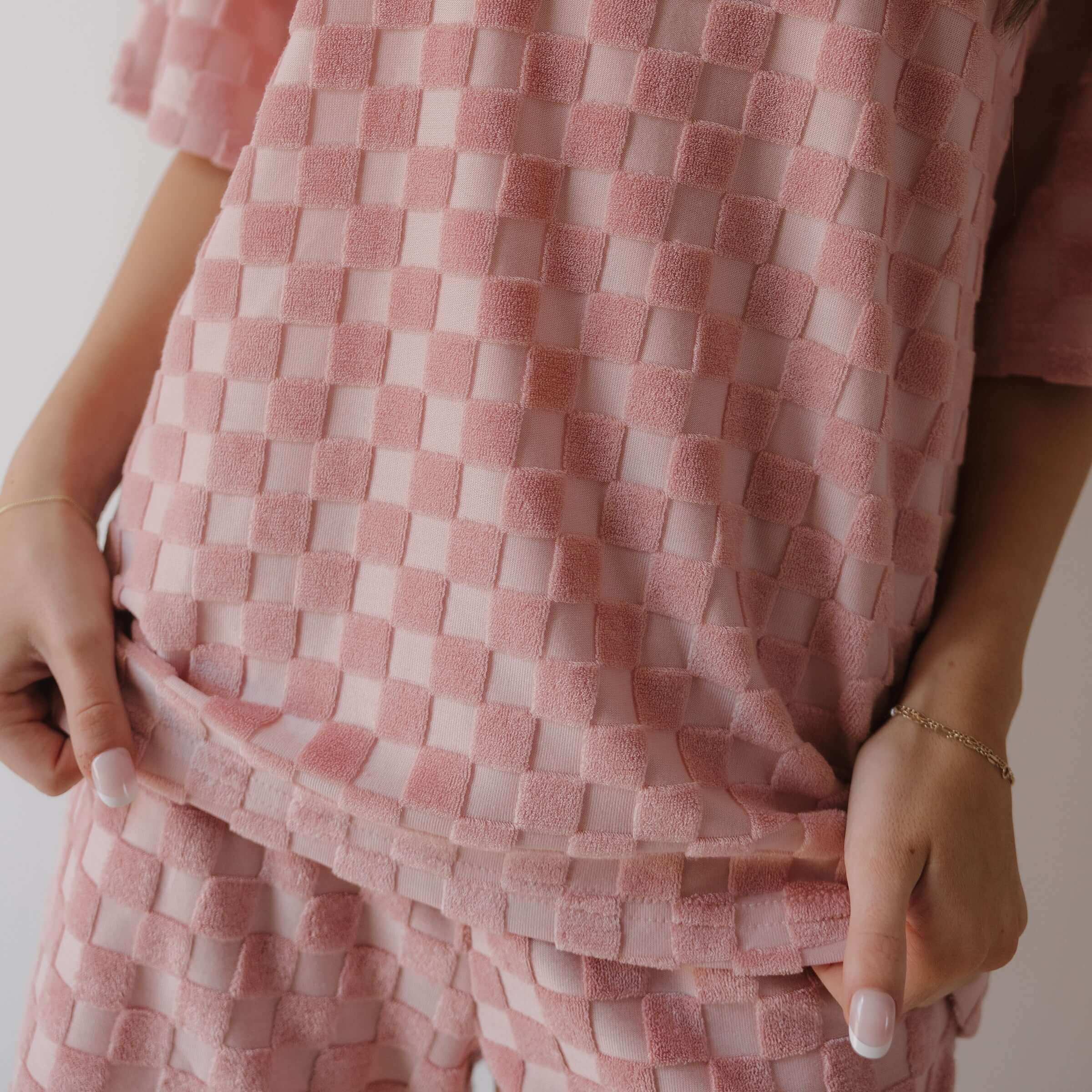 Close-up of a pink woven fabric garment with hands adjusting it.