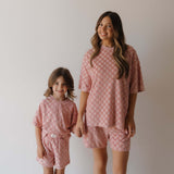 Two people wearing matching pink checkered outfits against a plain background