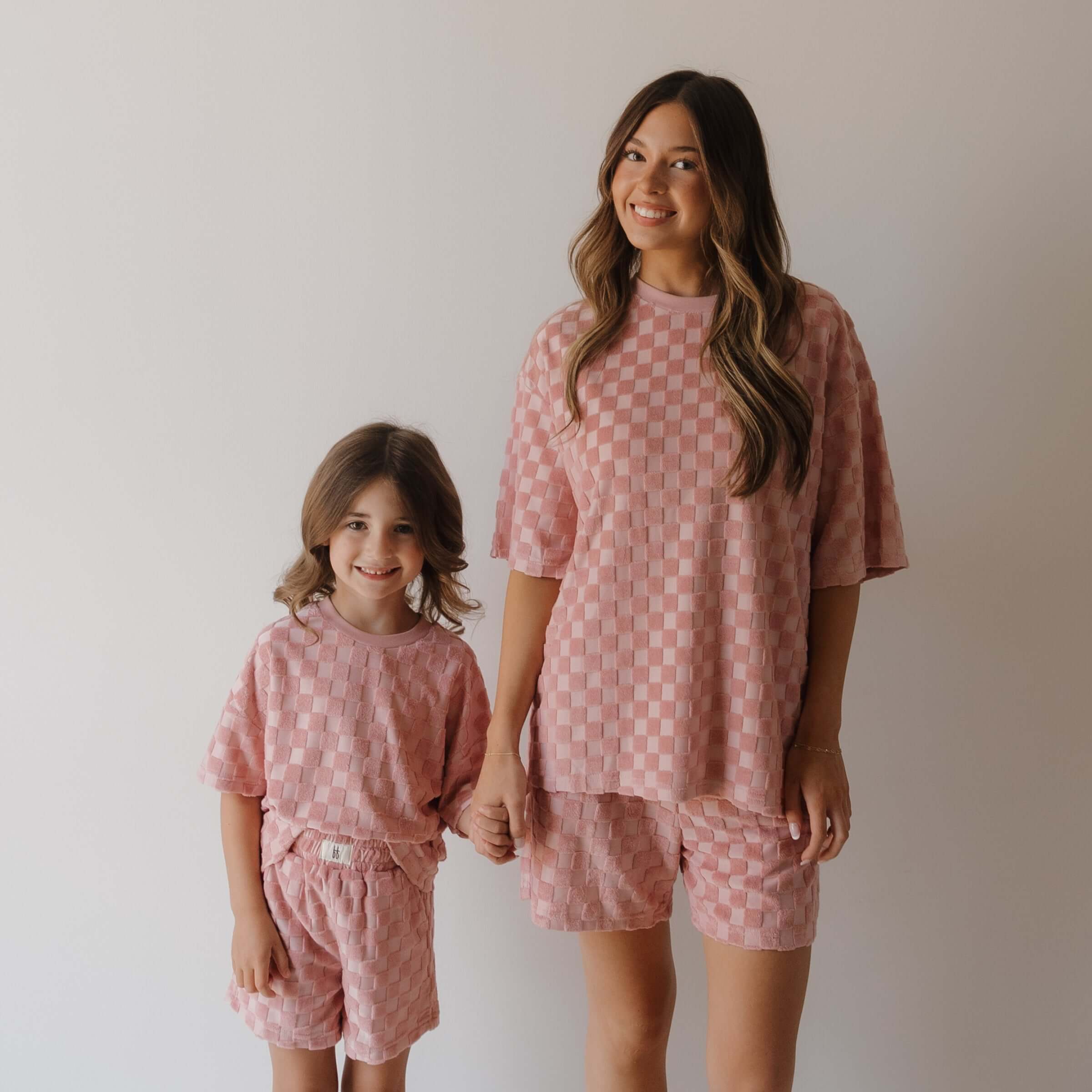 Two people wearing matching pink checkered outfits against a plain background