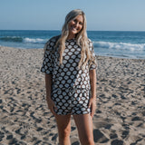 Women in Seashells Women's Bamboo Short Set on the beach, showcasing oversized t-shirt and drawstring shorts.