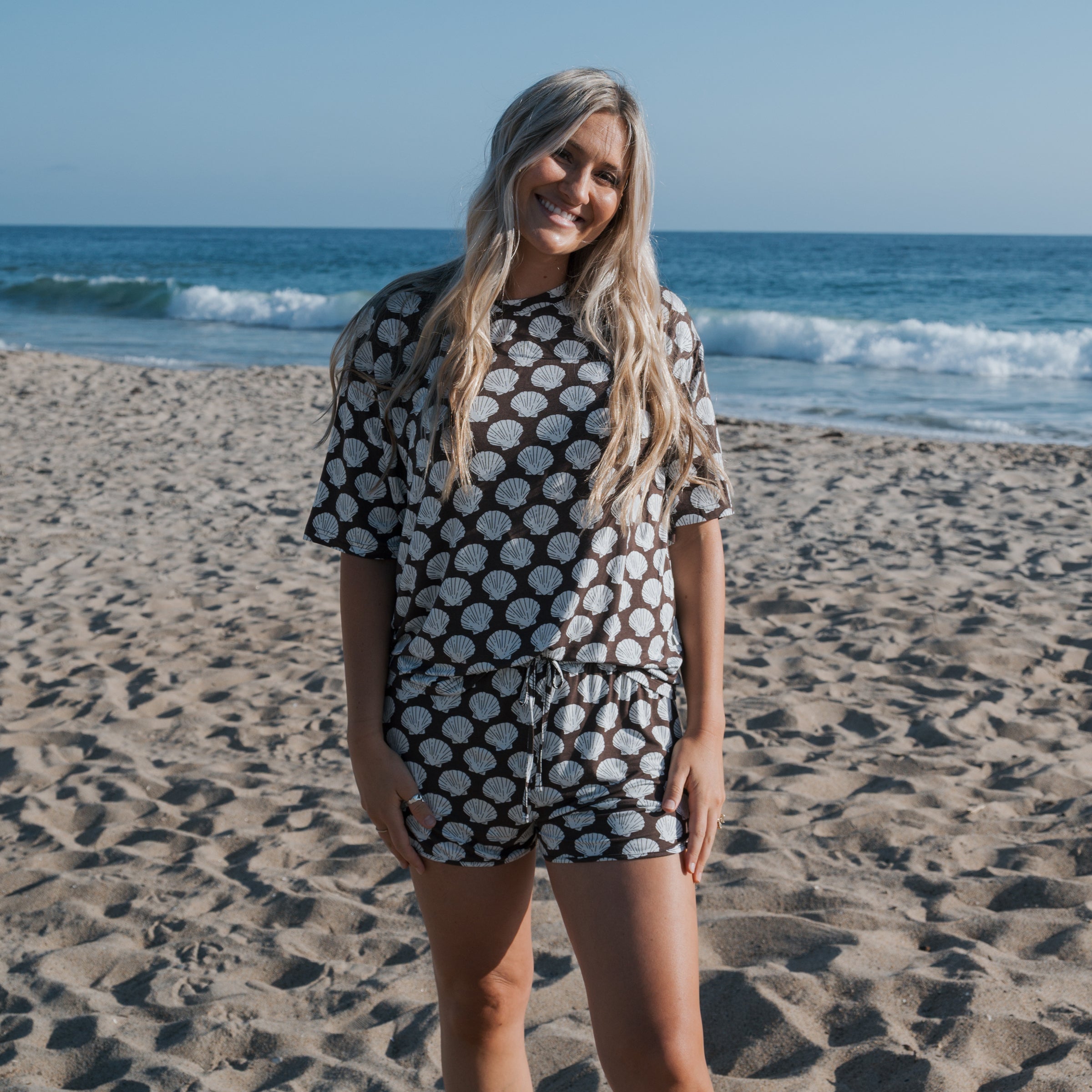 Women in Seashells Women's Bamboo Short Set on the beach, showcasing oversized t-shirt and drawstring shorts.