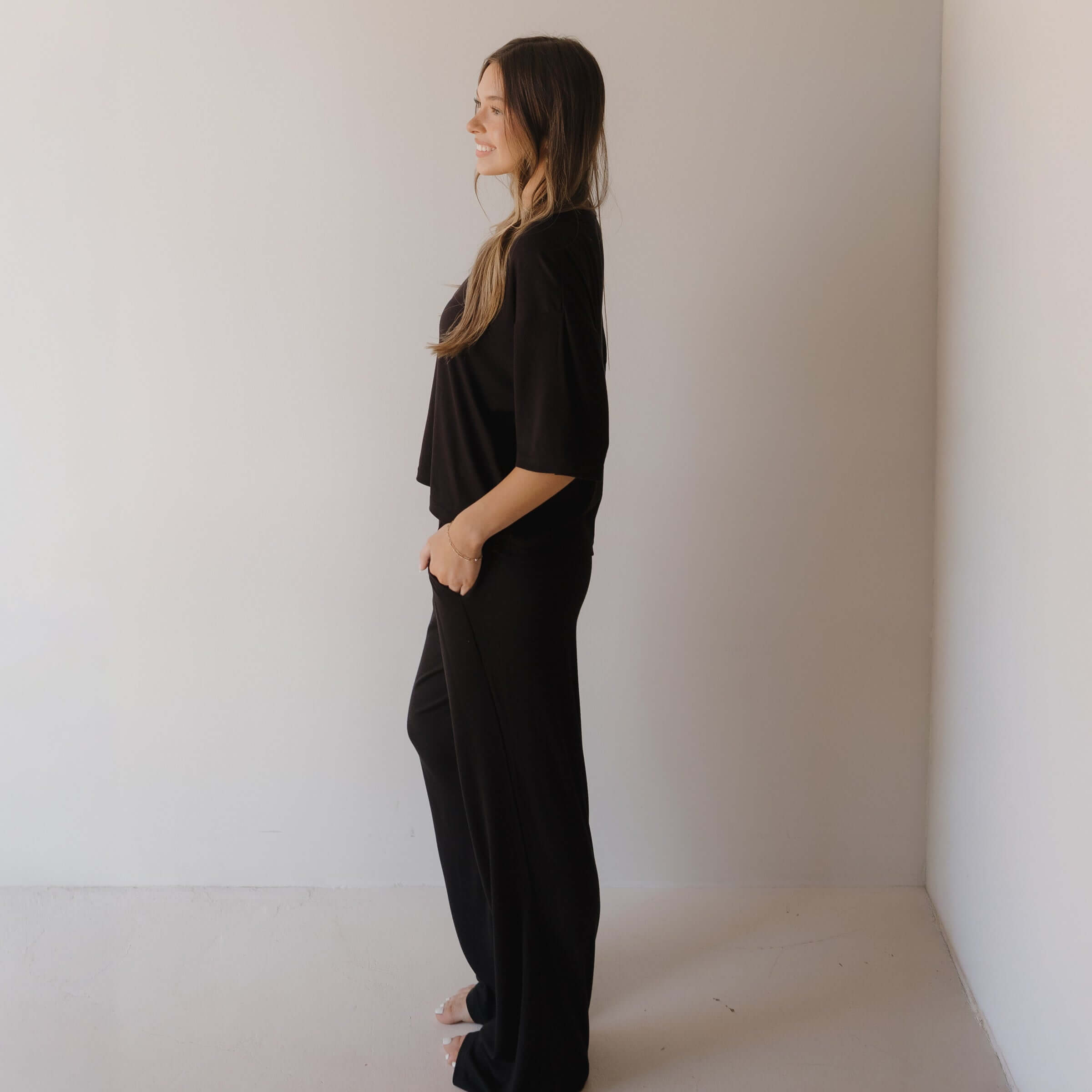 Woman wearing black pajamas standing against a plain wall.