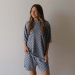 Woman wearing a matching gray blue checkered shirt and shorts set against a plain background