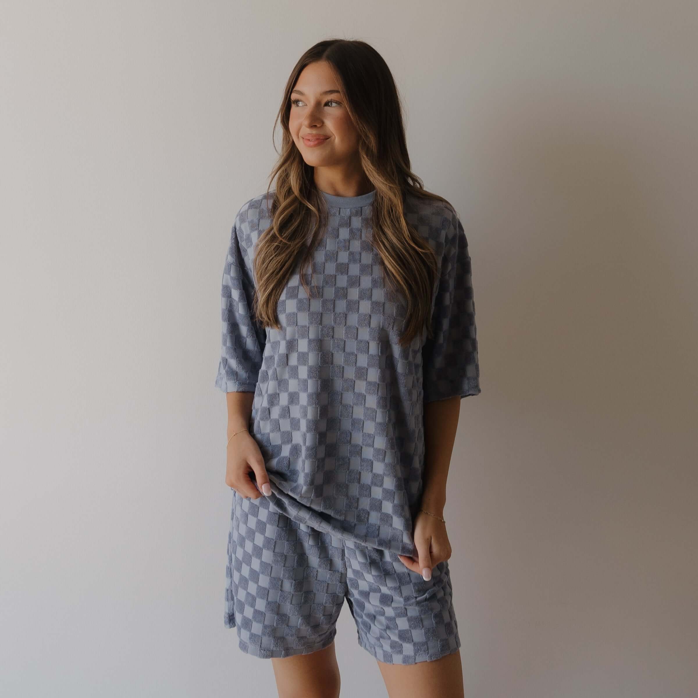 Woman wearing a matching gray blue checkered shirt and shorts set against a plain background