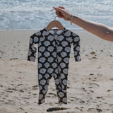 Baby onesie with shell pattern on a hanger against a beach background