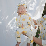 Baby wearing Lemon Bamboo Zip Pajamas with lemon print and headband, showcasing softness and comfort.