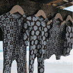 Collection of Summer Check Bamboo Zip Pajamas hanging on a wooden rack by the beach.