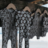 Patterned baby rompers hanging on wooden hangers with a blurred natural background