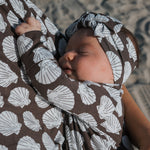 Newborn baby swaddled in a brown and white shell patterned blanket