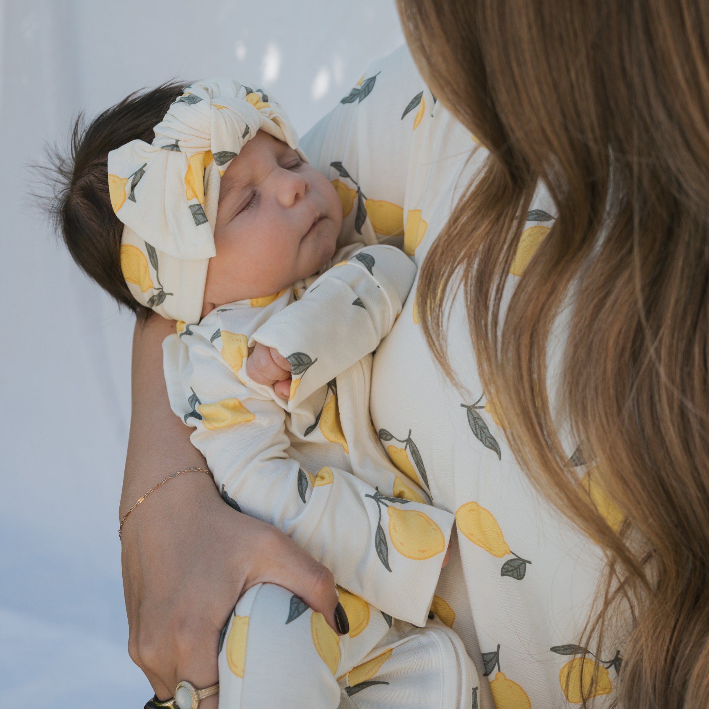 A baby wearing Lemon Bamboo Zip Pajamas with a matching headband, peacefully asleep in a caregiver's arms.