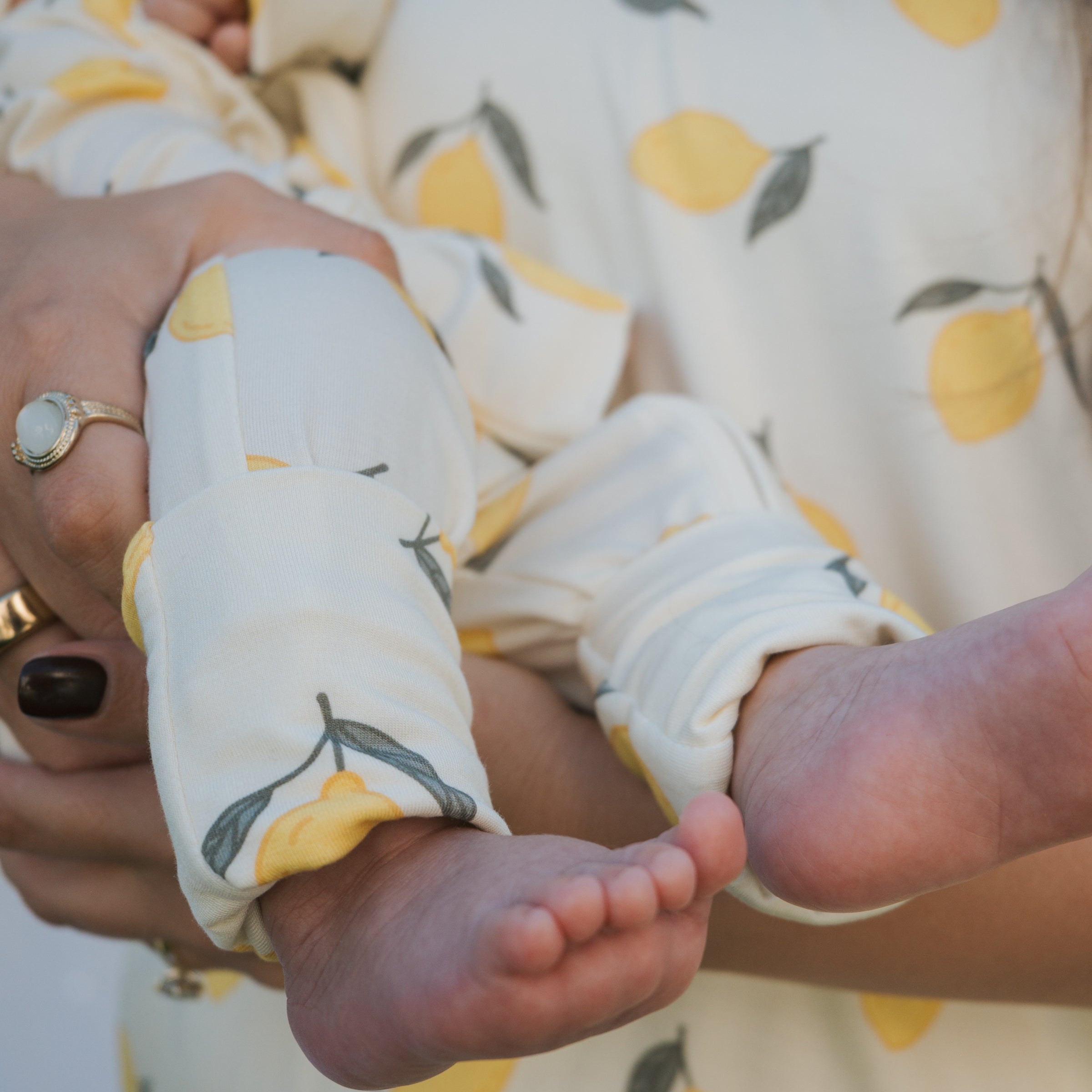 A close-up of a baby in Lemon Bamboo Zip Pajamas with rollover cuffs, showcasing soft bamboo fabric and a playful lemon pattern.