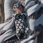 Newborn baby wrapped in a brown and white patterned blanket on a textured surface