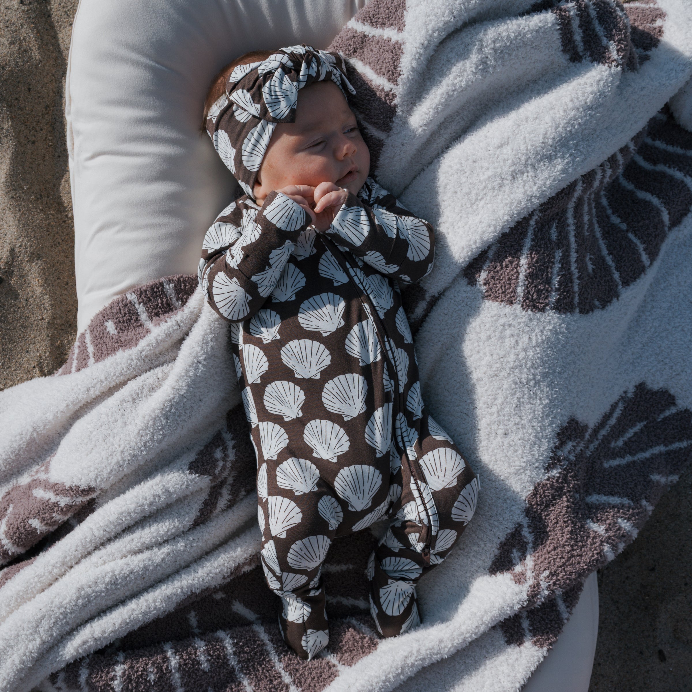 Newborn baby wrapped in a brown and white patterned blanket on a textured surface