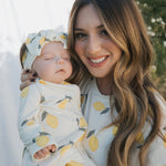 Woman holding a baby both wearing lemon-patterned outfits outdoors.