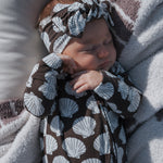 Baby wrapped in a brown and white shell patterned blanket with matching headband.