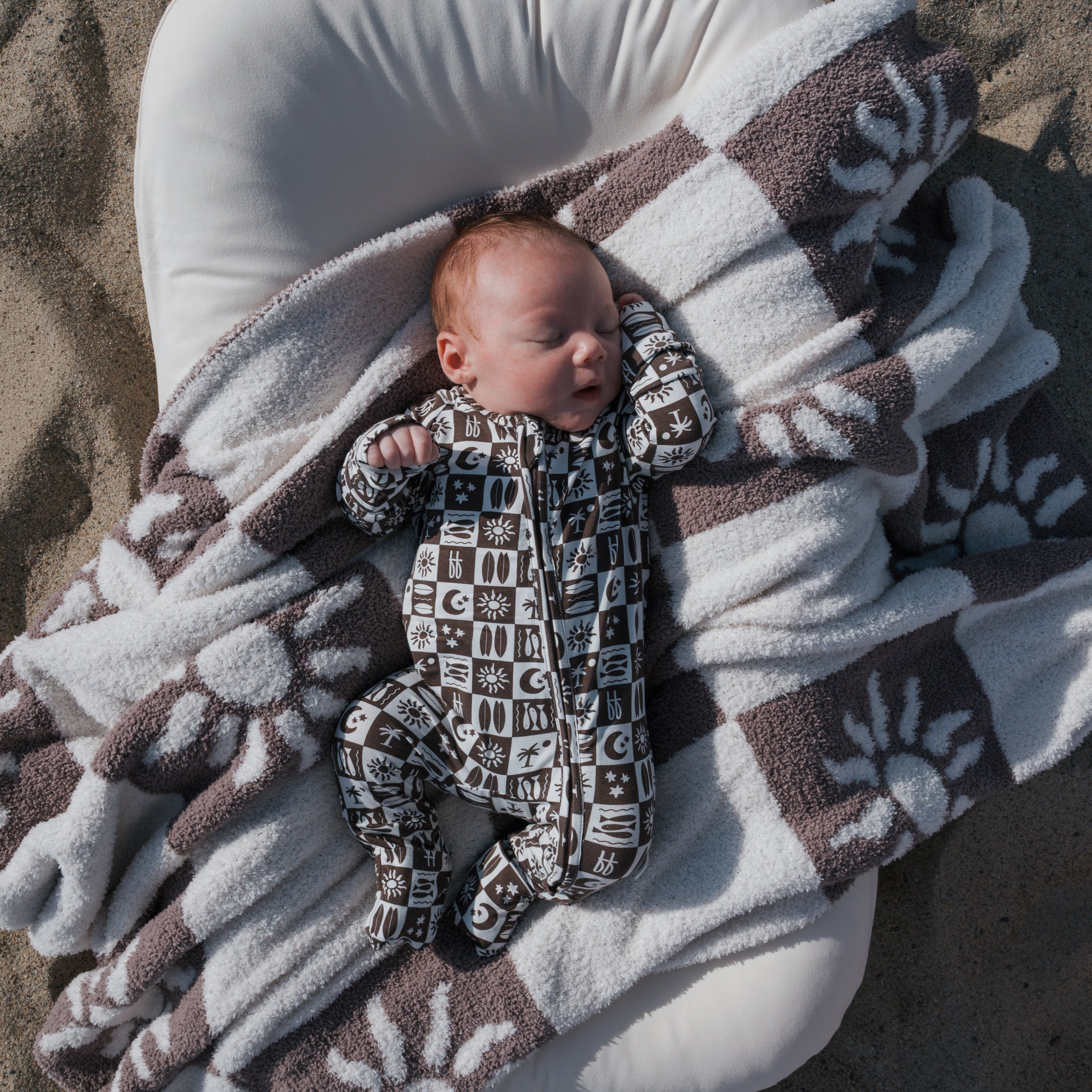 Baby sleeping on a blanket wearing Bamboo Zip Pajamas with playful designs, enjoying cozy comfort.